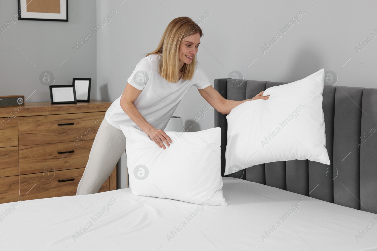 Photo of Woman putting pillows on bed at home. Domestic chores