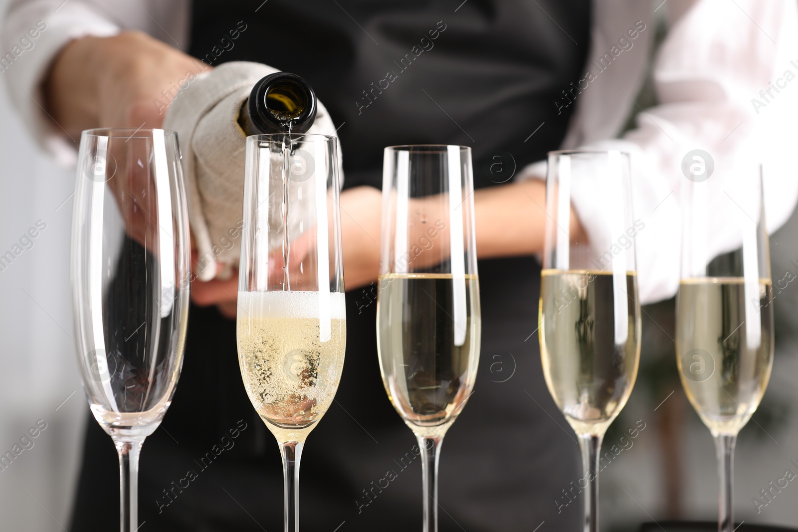 Photo of Waiter filling glasses with champagne indoors, closeup