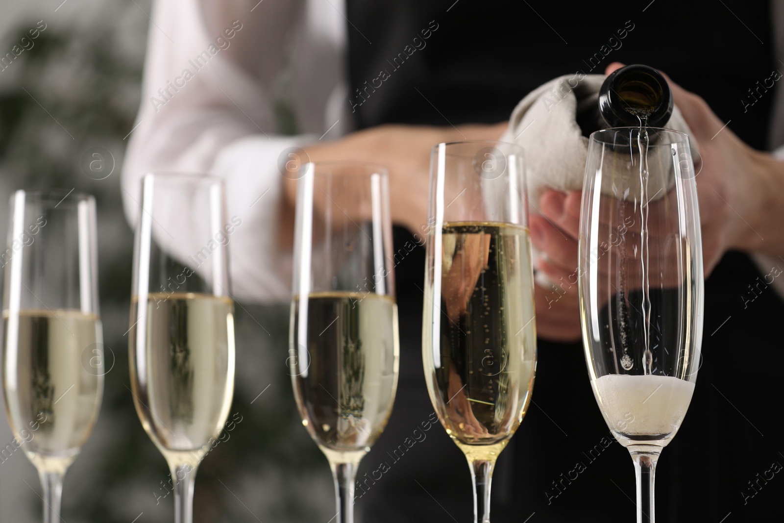 Photo of Waiter filling glasses with champagne indoors, closeup