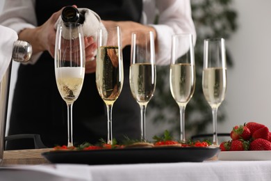 Photo of Waiter filling glasses with champagne indoors, closeup