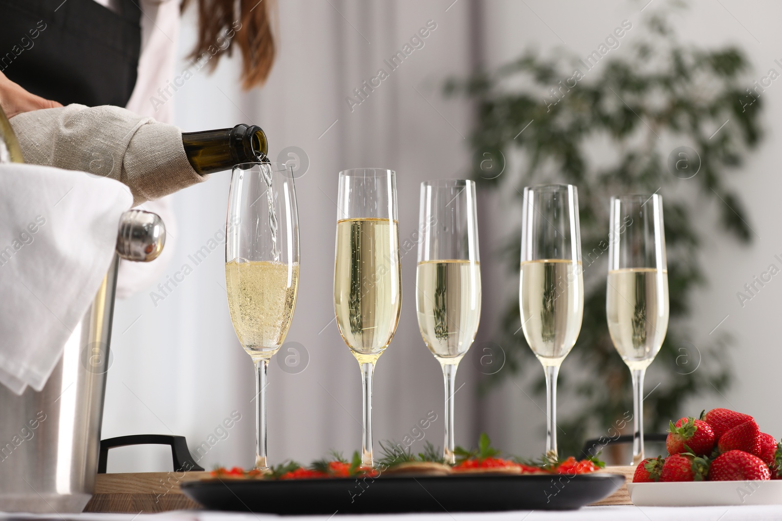 Photo of Waiter filling glasses with champagne indoors, closeup