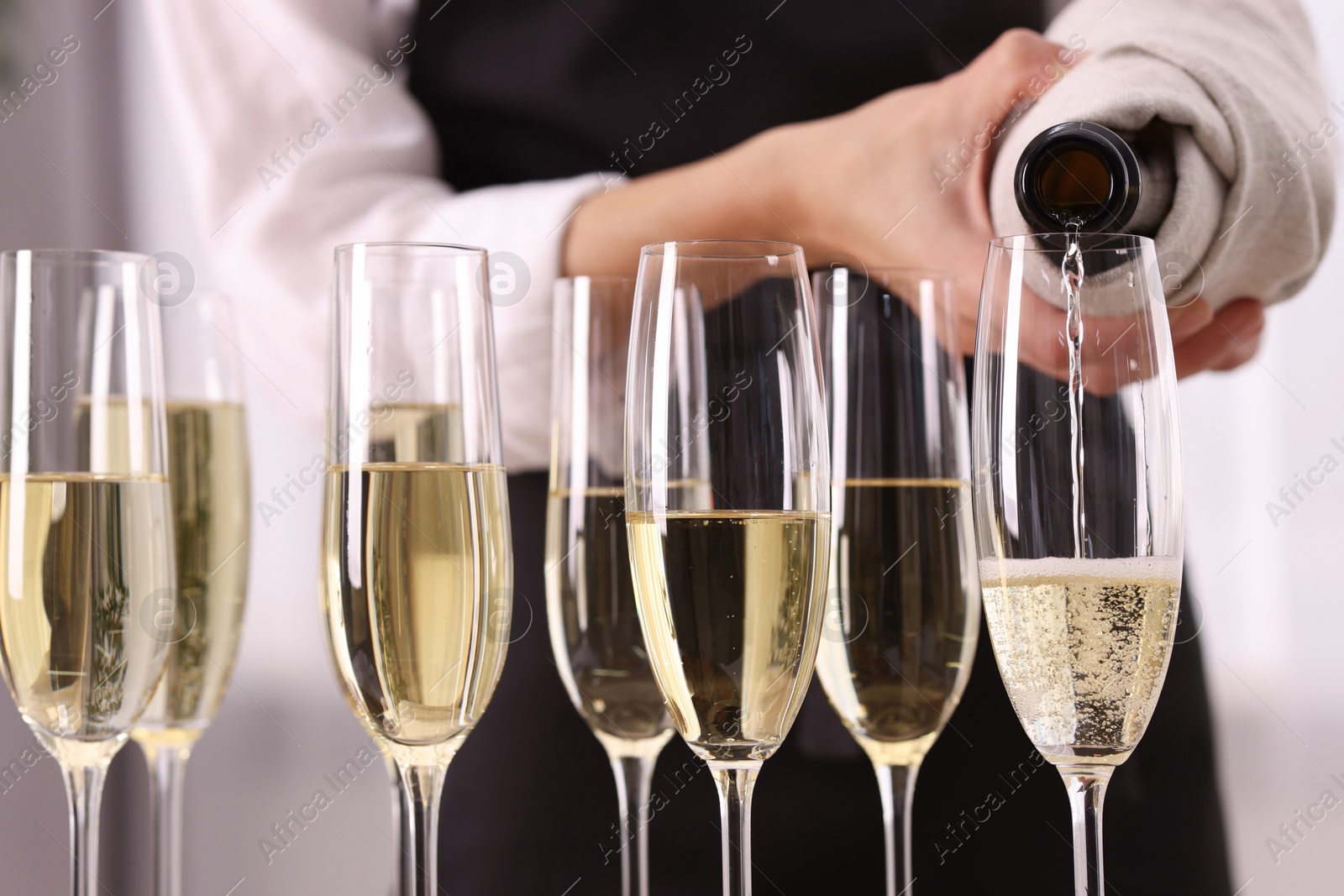 Photo of Waiter filling glasses with champagne indoors, closeup