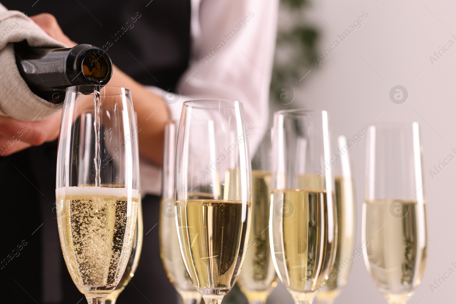 Photo of Waiter filling glasses with champagne indoors, closeup