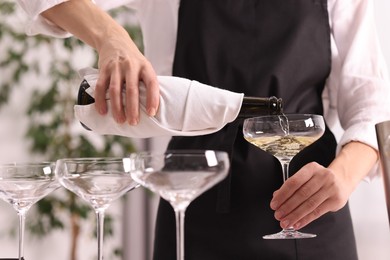 Photo of Waiter filling glasses with champagne indoors, closeup