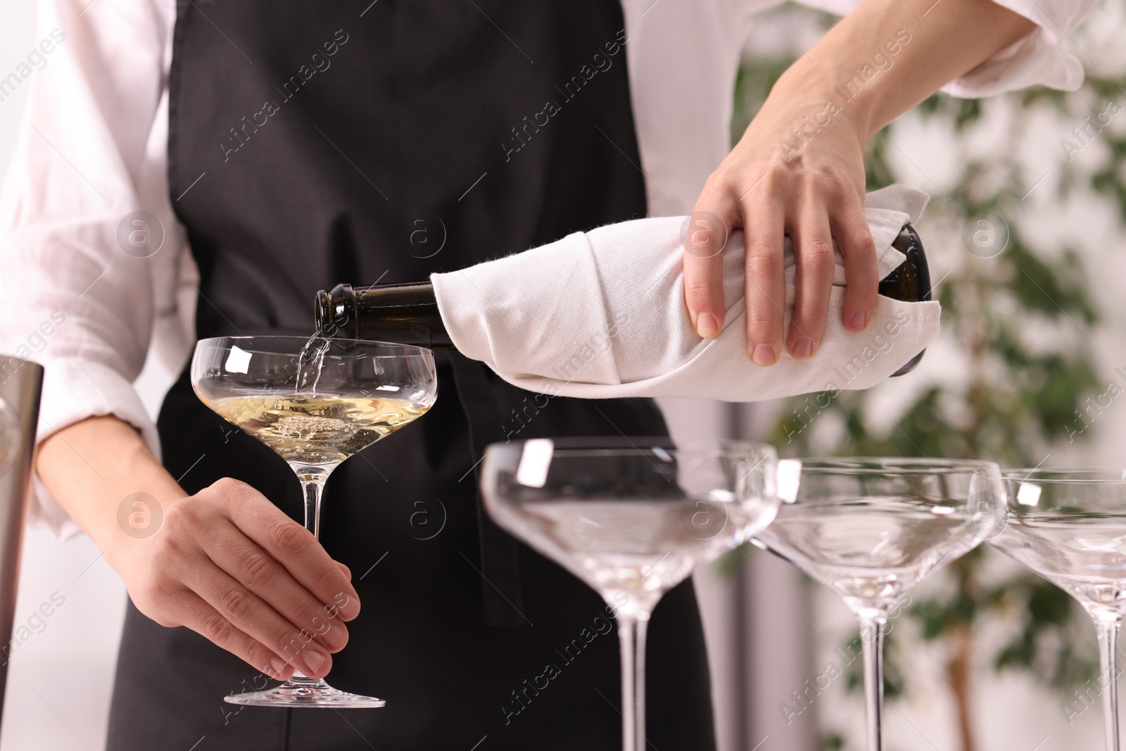 Photo of Waiter filling glasses with champagne indoors, closeup