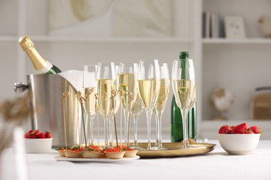 Photo of Champagne, strawberries and canapes with red caviar on white table indoors