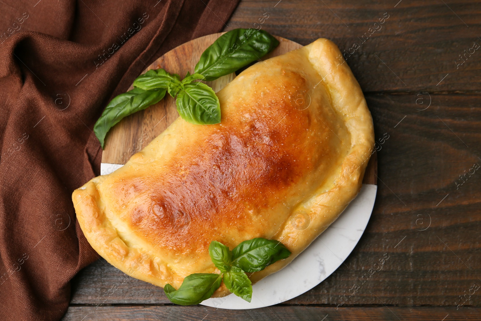 Photo of Tasty vegetarian calzone with basil on wooden table, top view