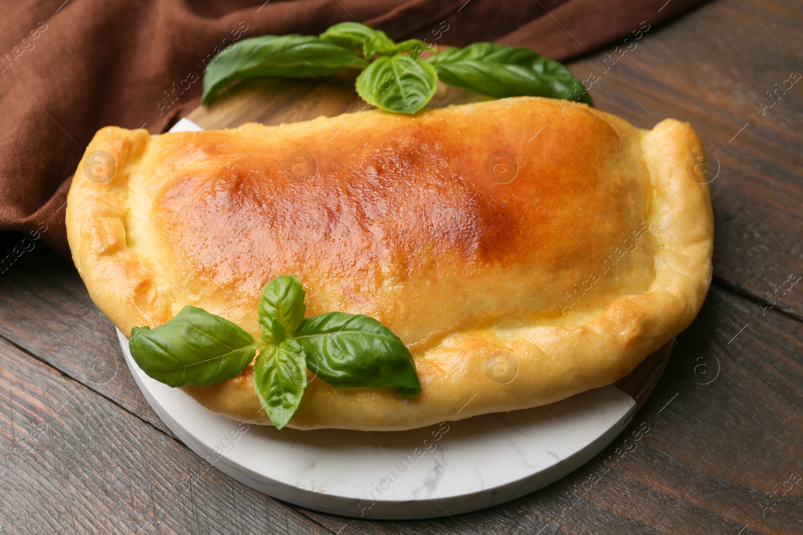 Photo of Tasty vegetarian calzone with basil on wooden table, closeup