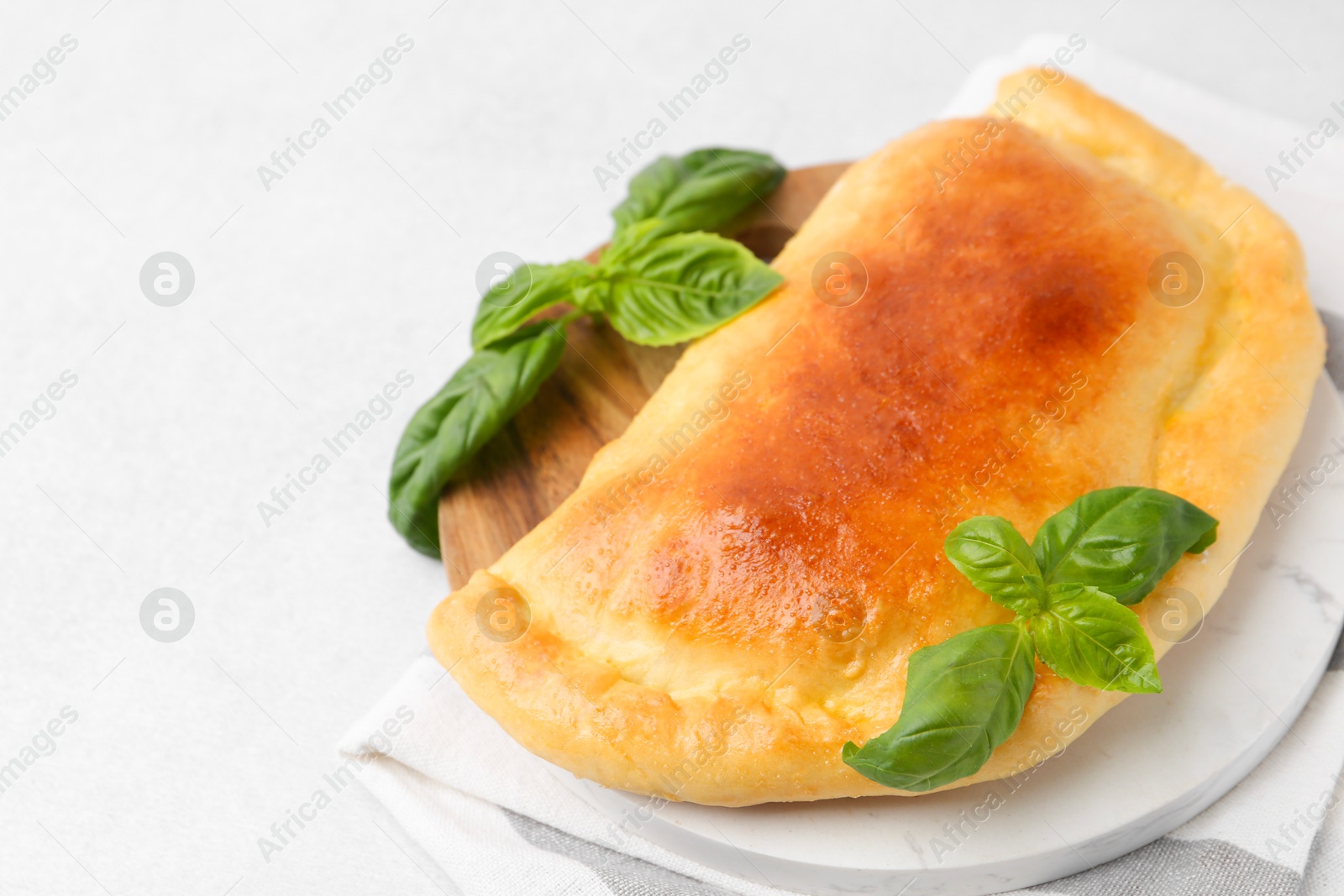 Photo of Tasty vegetarian calzone with basil on light table, closeup. Space for text