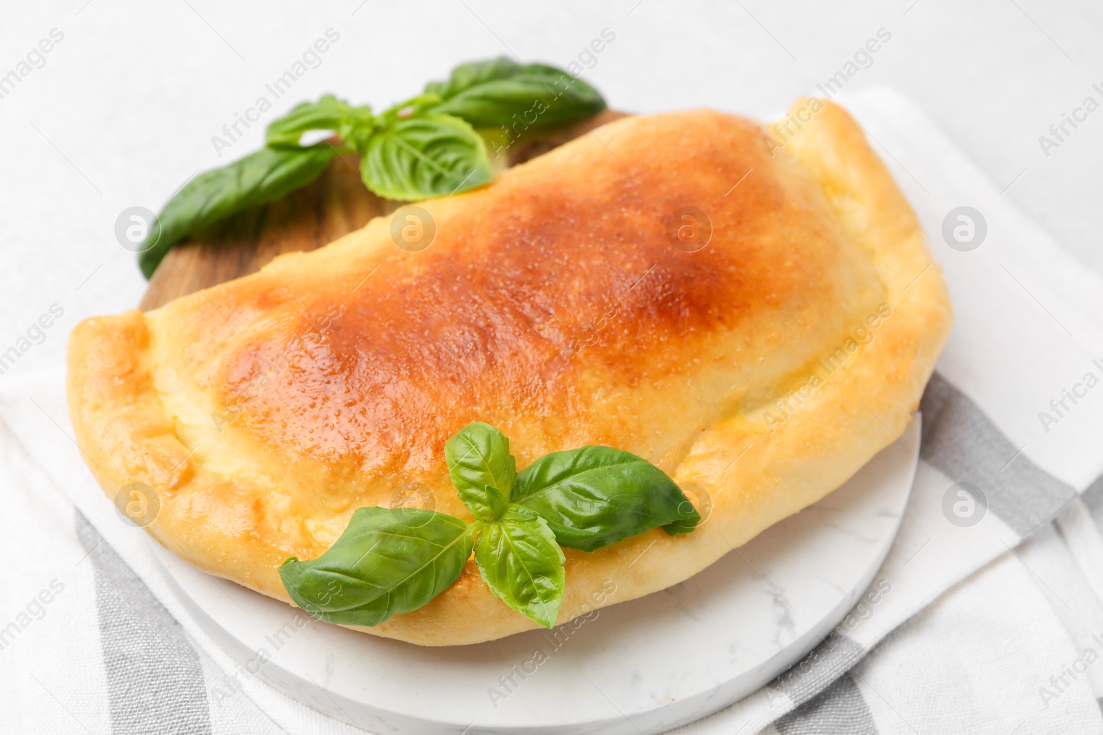 Photo of Tasty vegetarian calzone with basil on light table, closeup