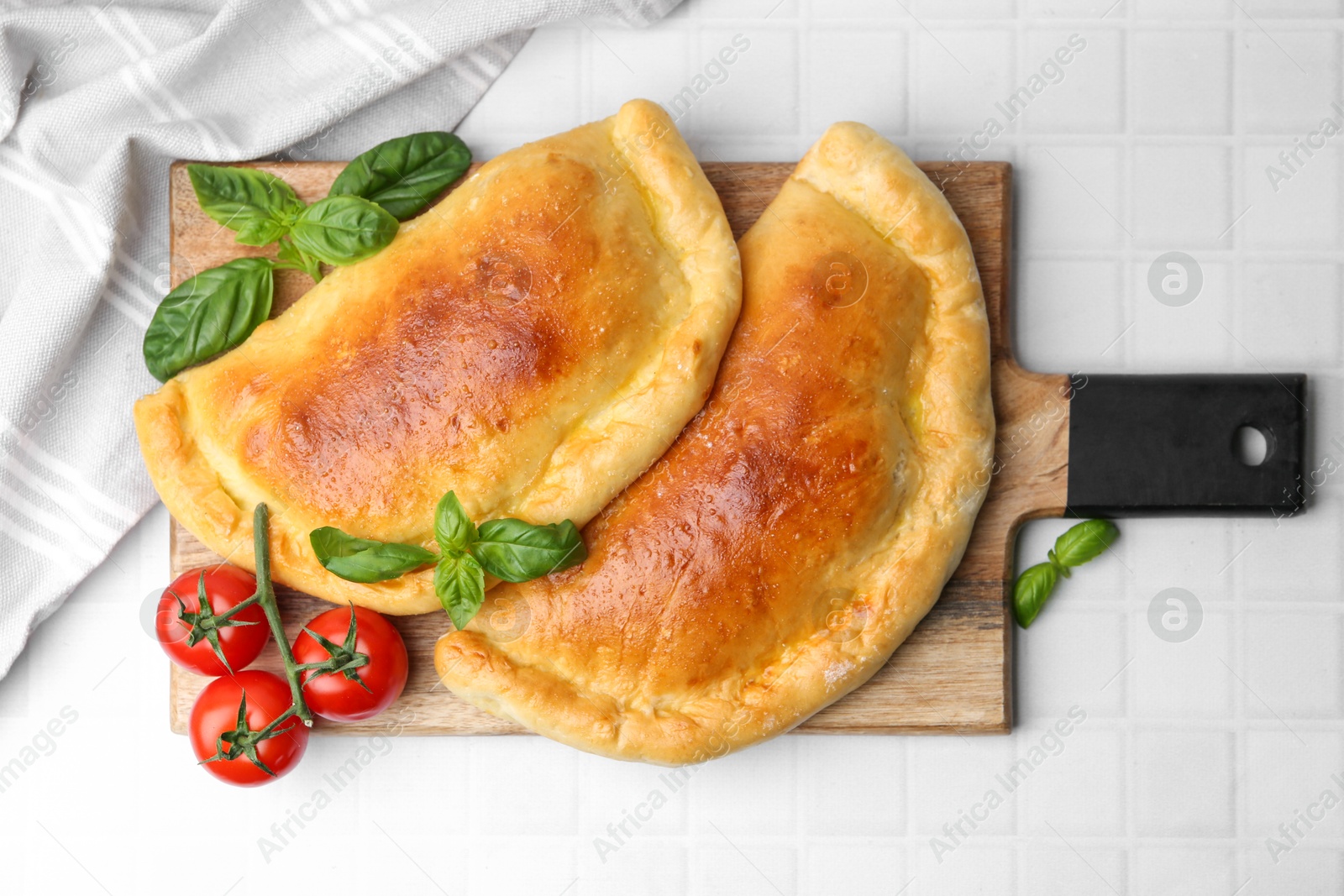 Photo of Tasty vegetarian calzones with basil and tomatoes on white tiled table, top view