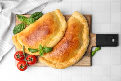 Photo of Tasty vegetarian calzones with basil and tomatoes on white tiled table, top view