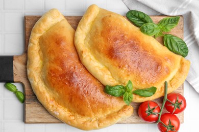 Photo of Tasty vegetarian calzones with basil and tomatoes on white tiled table, top view