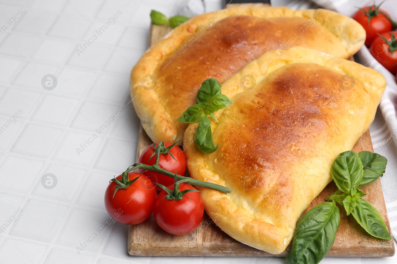 Photo of Tasty vegetarian calzones with basil and tomatoes on white tiled table, closeup. Space for text