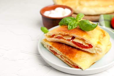 Photo of Pieces of tasty vegetarian calzone with tomato, cheese and basil on white textured table, closeup. Space for text