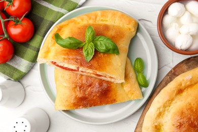 Photo of Pieces of tasty vegetarian calzone with tomatoes, mozzarella cheese and basil on white textured table, top view