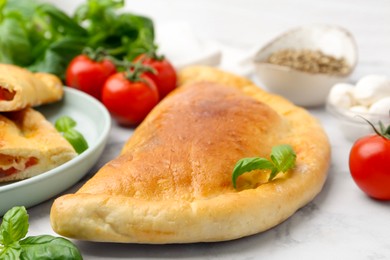 Photo of Tasty vegetarian calzone with tomatoes, mozzarella cheese and spices on white marble table, closeup