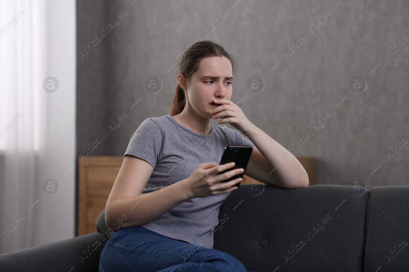 Photo of Depressed woman calling hotline for mental health help on sofa at home