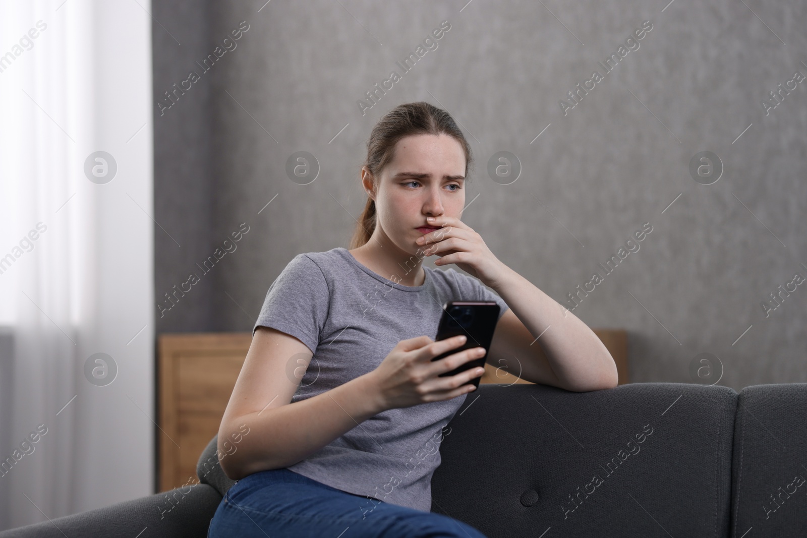 Photo of Depressed woman calling hotline for mental health help on sofa at home