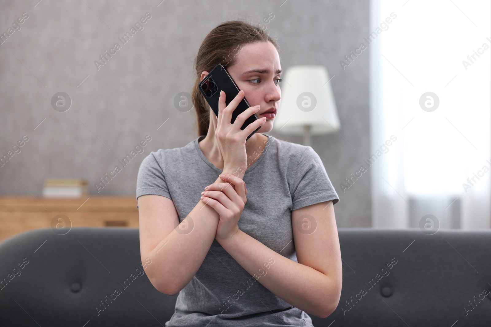 Photo of Depressed woman calling hotline for mental health help on sofa at home