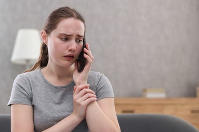 Photo of Depressed woman calling hotline for mental health help on sofa at home. Space for text