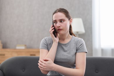 Photo of Depressed woman calling hotline for mental health help on sofa at home