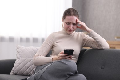 Photo of Depressed woman calling hotline for mental health help on sofa at home