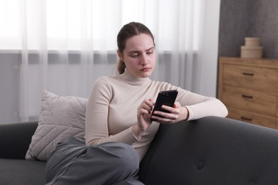 Photo of Depressed woman calling hotline for mental health help on sofa at home