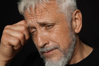 Photo of Sad senior man crying on black background, closeup