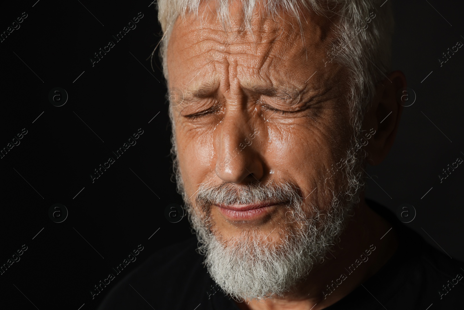 Photo of Sad senior man crying on black background, closeup. Space for text