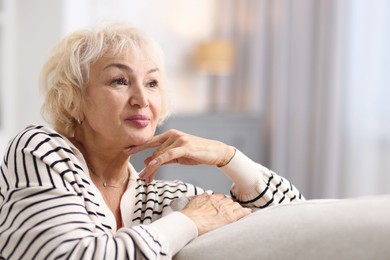 Photo of Beautiful grandmother sitting on sofa at home. Space for text