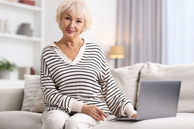 Photo of Beautiful grandmother using laptop on sofa at home