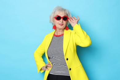 Photo of Portrait of fashionable grandmother in sunglasses and yellow jacket on light blue background