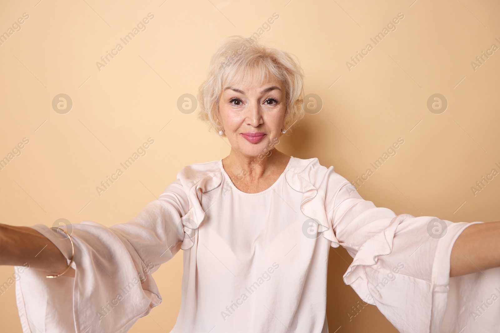 Photo of Elegant grandmother taking selfie on beige background