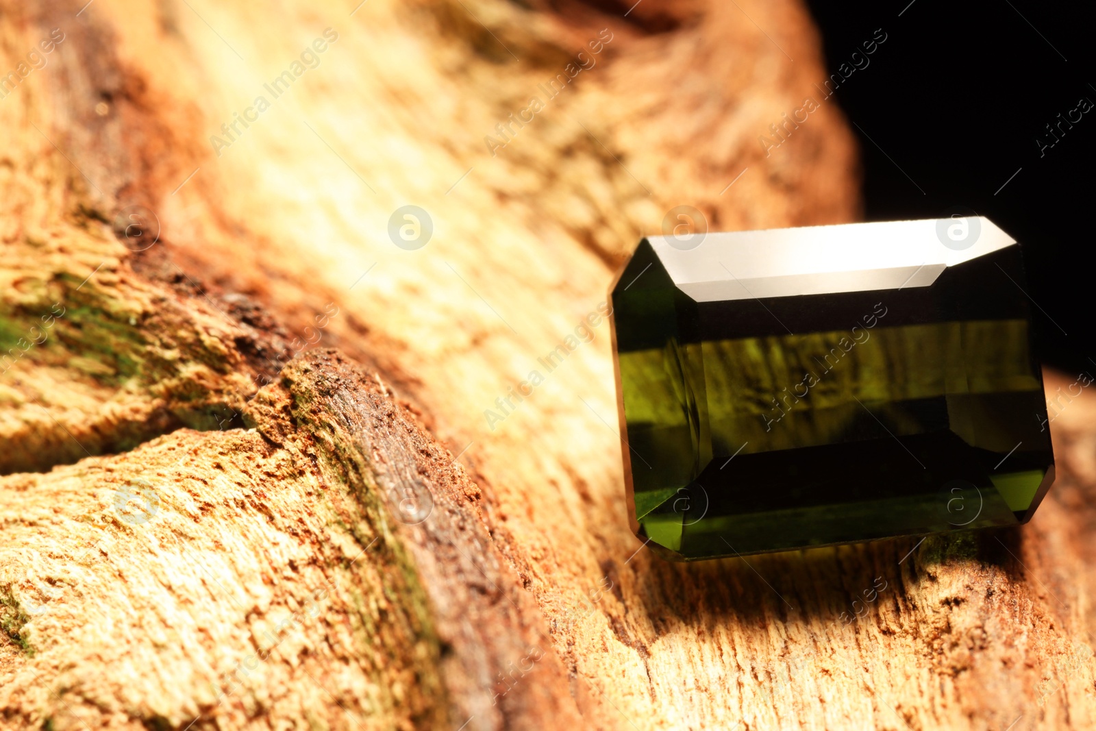 Photo of Beautiful shiny green gemstone on stone, closeup. Space for text