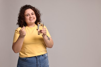 Photo of Happy plus size woman with weight loss supplements and glass of water on grey background. Space for text