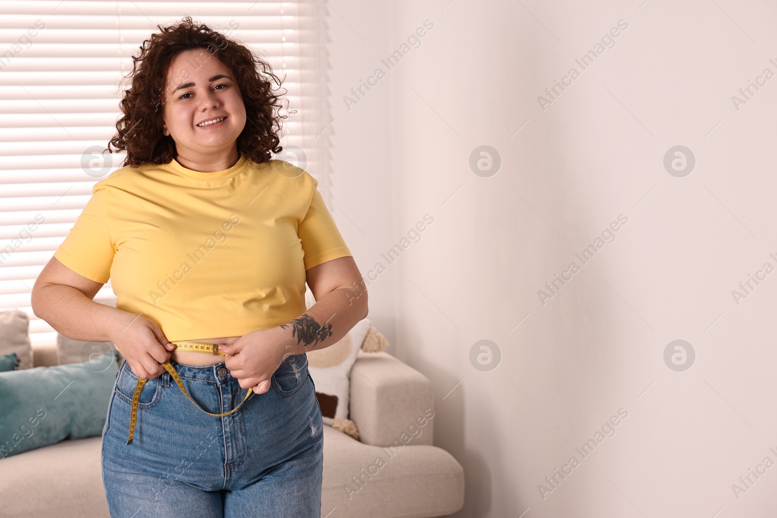 Photo of Weight loss. Happy plus size woman measuring waist with tape at home. Space for text