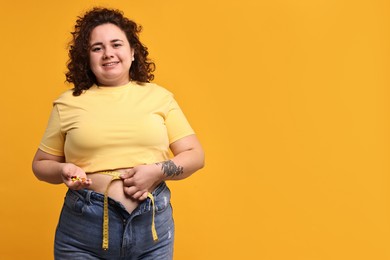 Photo of Happy plus size woman measuring waist with tape and holding pile of weight loss supplements on orange background. Space for text