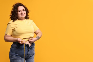 Photo of Happy plus size woman measuring waist with tape and holding pile of weight loss supplements on orange background. Space for text