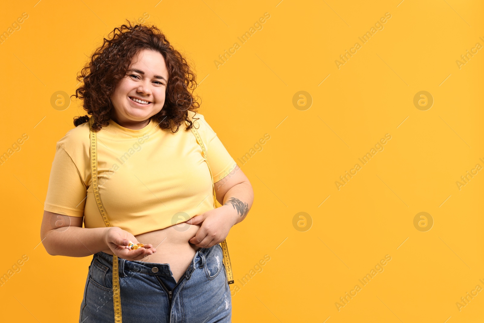 Photo of Happy plus size woman with pile of weight loss supplements on orange background. Space for text