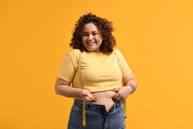 Happy plus size woman with pile of weight loss supplements on orange background