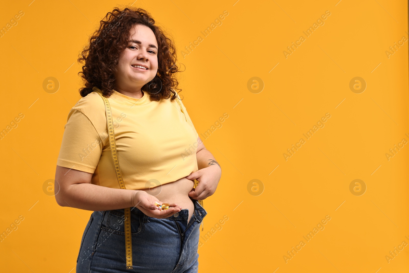 Photo of Happy plus size woman with pile of weight loss supplements on orange background. Space for text