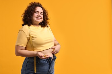 Photo of Happy plus size woman with pile of weight loss supplements on orange background. Space for text