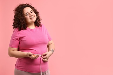 Photo of Happy plus size woman measuring waist with tape and holding pile of weight loss supplements on pink background. Space for text