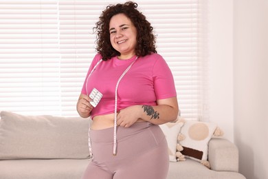 Happy plus size woman holding blister of weight loss supplements at home