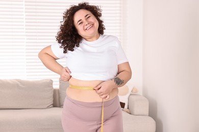 Photo of Weight loss. Happy plus size woman measuring waist with tape at home