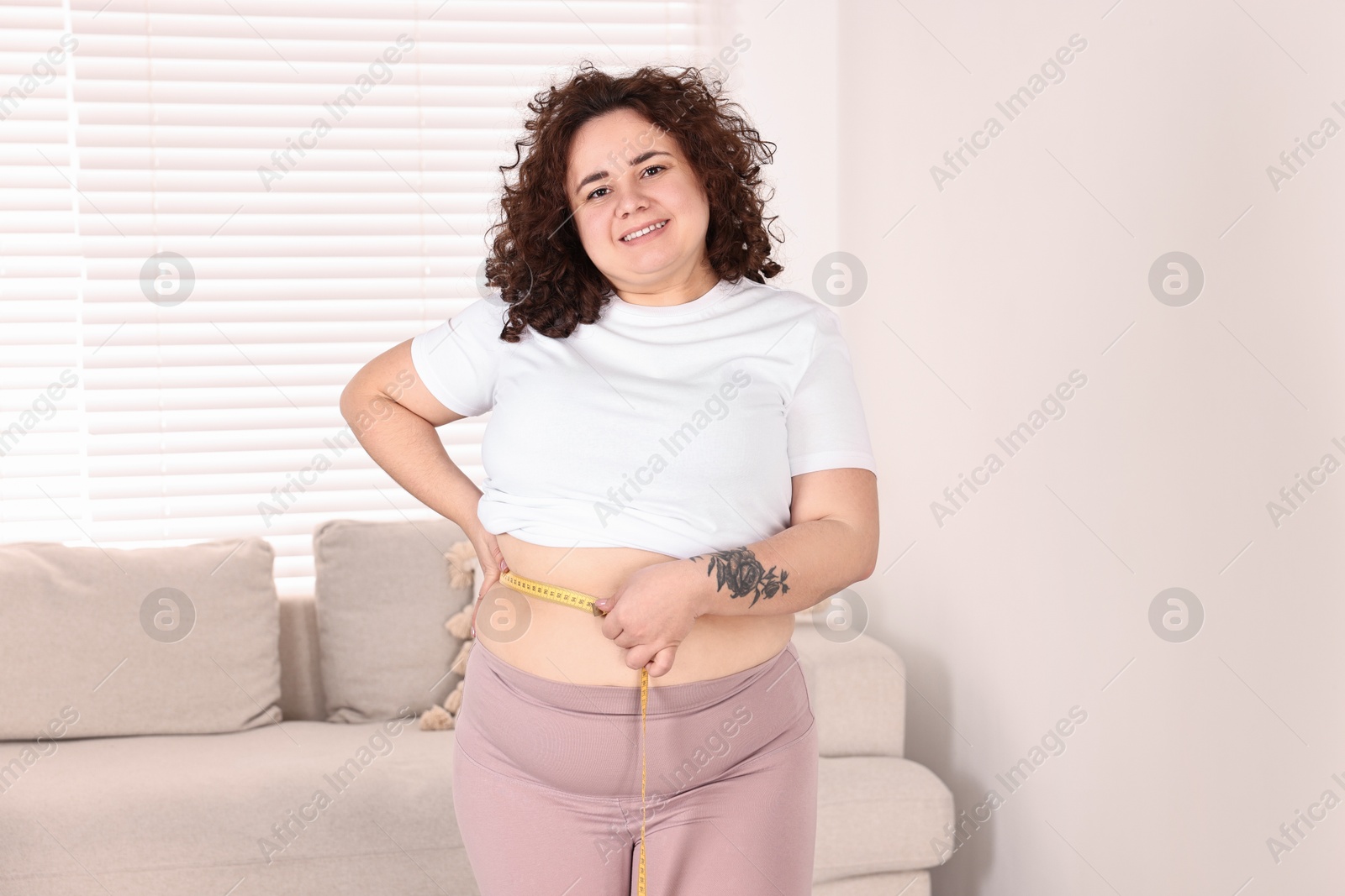 Photo of Weight loss. Happy plus size woman measuring waist with tape at home