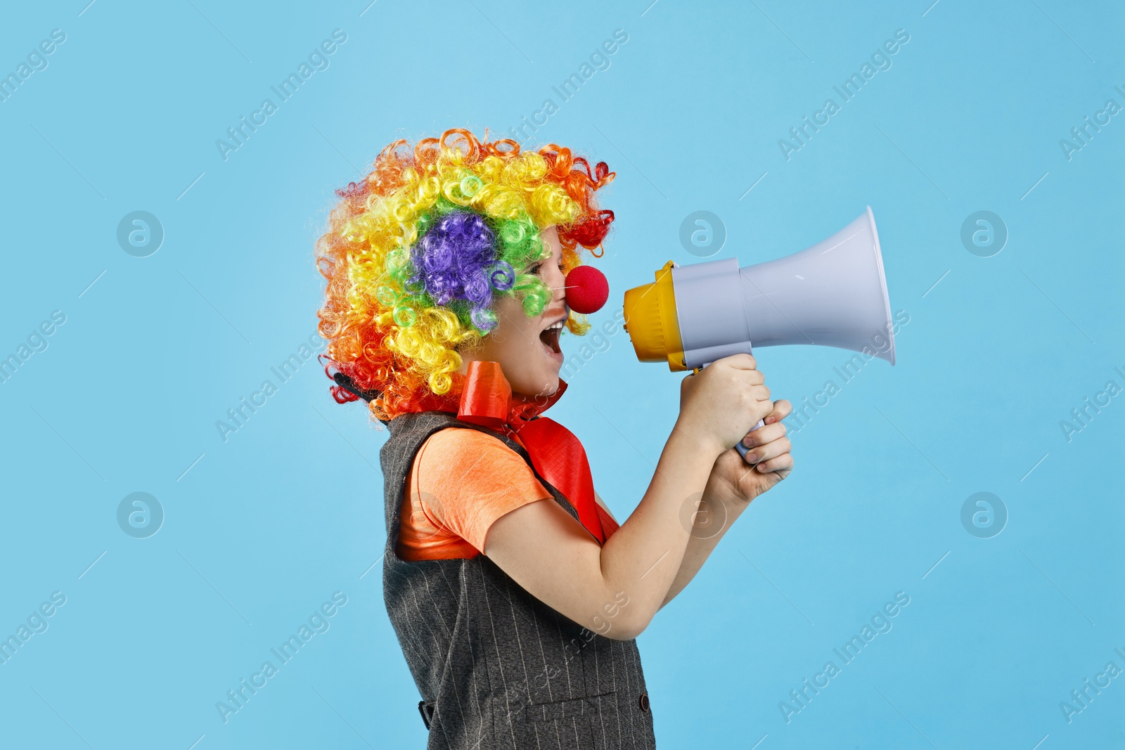 Photo of Little boy dressed like clown shouting in megaphone on light blue background. Surprise party