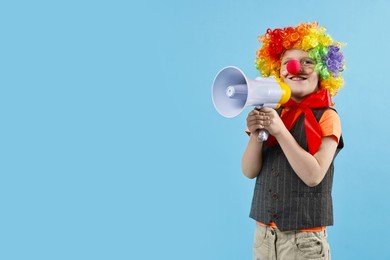 Photo of Happy little boy dressed like clown with megaphone on light blue background, space for text. Surprise party