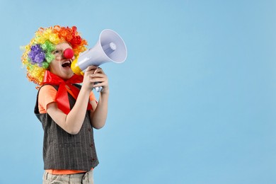 Photo of Little boy dressed like clown shouting in megaphone on light blue background, space for text. Surprise party